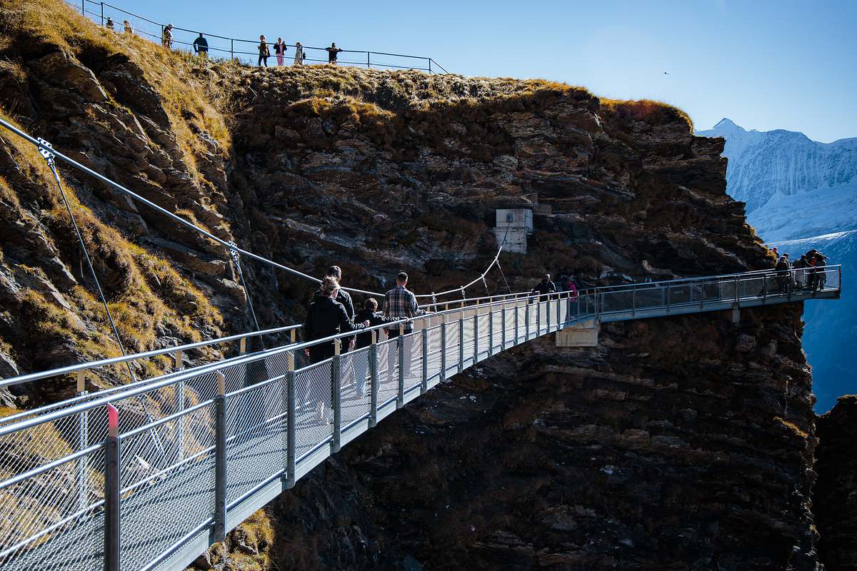 Metallsteg des First Cliff Walk ragt &uuml;ber die Felskante hinaus, mit Wanderern auf dem Gipfelplateau und Bergpanorama im Hintergrund an einem sonnigen Herbsttag