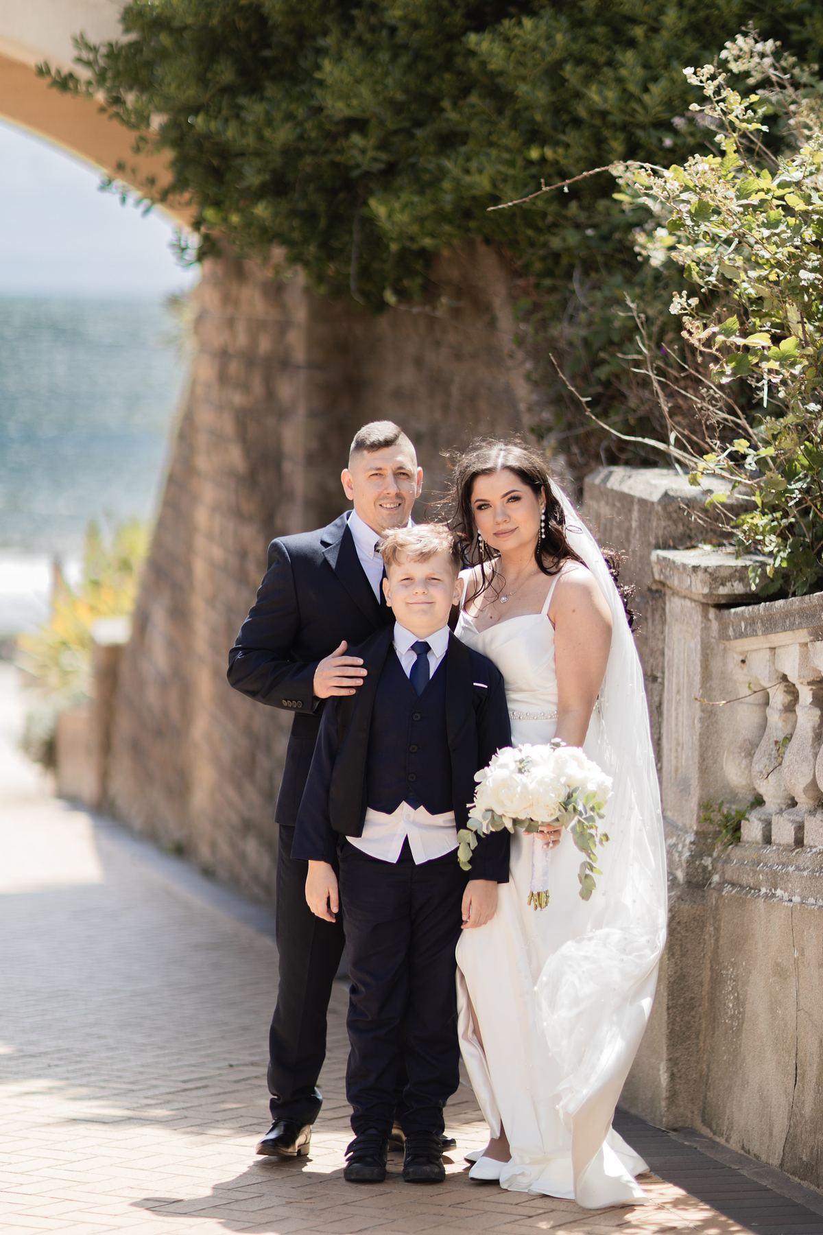 Bride and groom with a young boy beside the seafront at Barry Island, South Wales