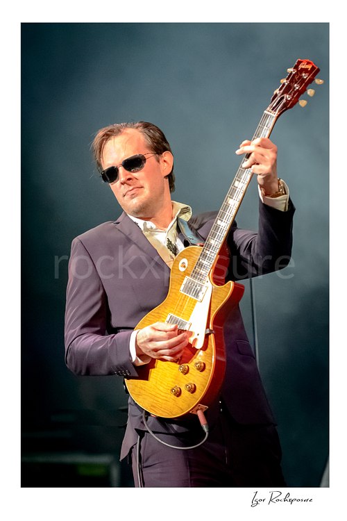 Vertical color image of Joe Bonamassa performing live on stage with his guitar in a striking concert portrait
