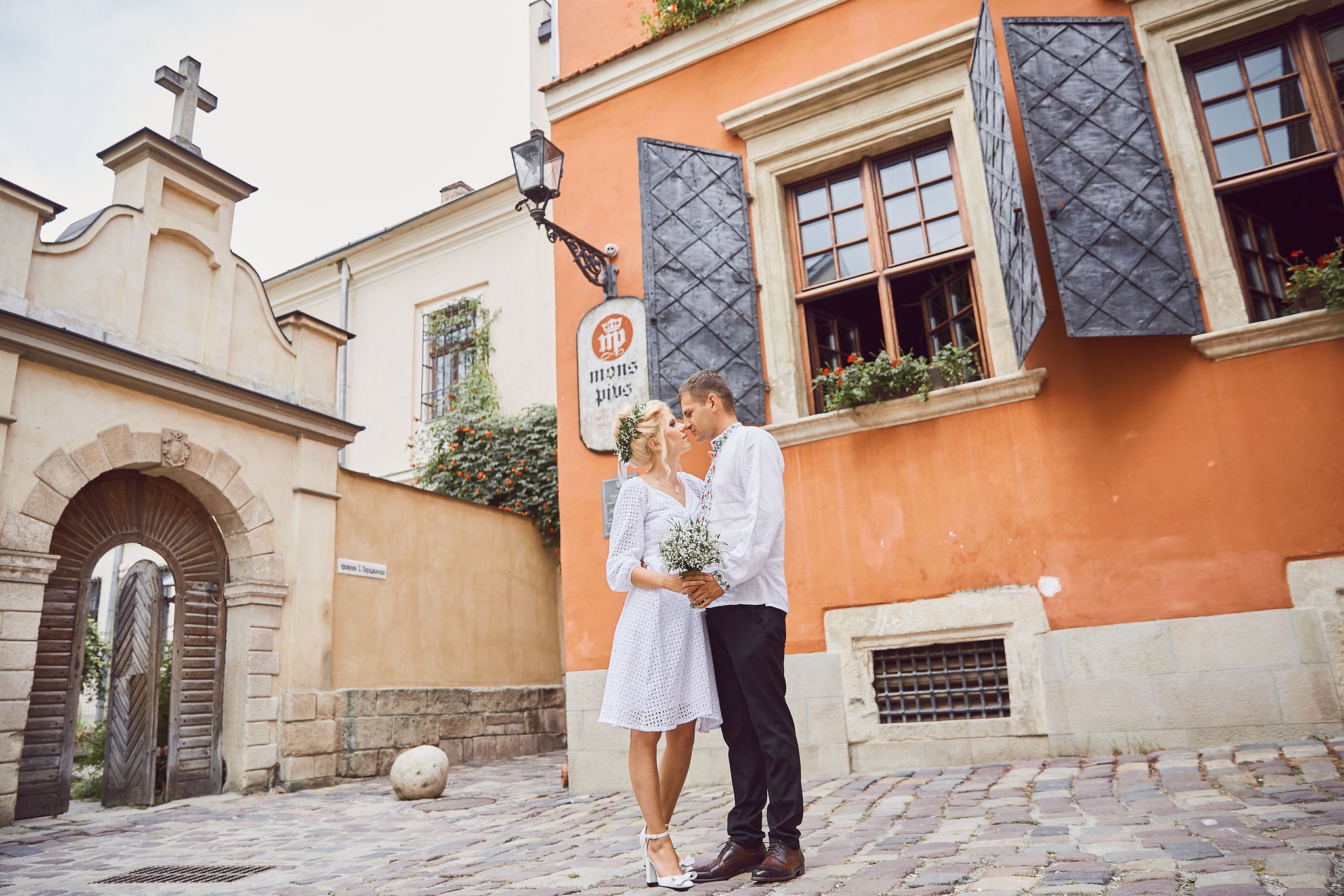 Bride and groom kissing beside colourful historic architecture in Lviv