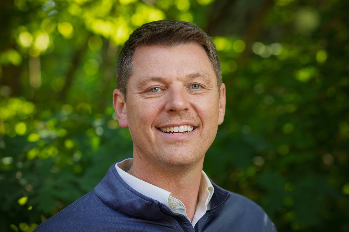 A man poses for a headshot with a natural background in Durham, NC