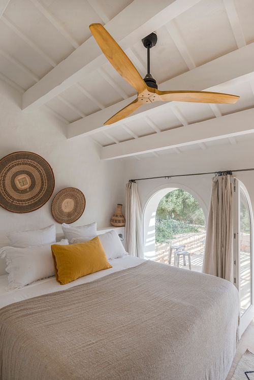 Chambre lumineuse avec lit, ventilateur de plafond et arches ouvertes sur l’extérieur dans la finca Son Fonoll à Minorque. Photographie par Nicolas Karadimos.