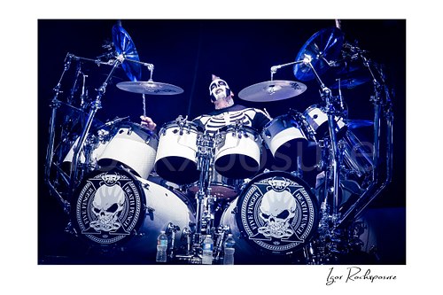 Horizontal color image of Jeremy Spencer of Five Finger Death Punch in an aerial overhead drummer shot behind a white drum kit under blue concert light