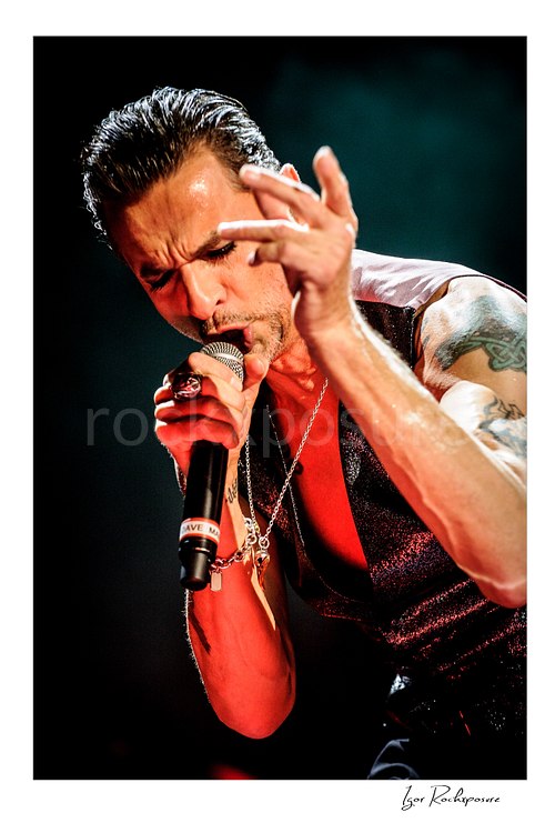 Vertical color image of Depeche Mode singer Dave Gahan singing into a microphone during a live performance