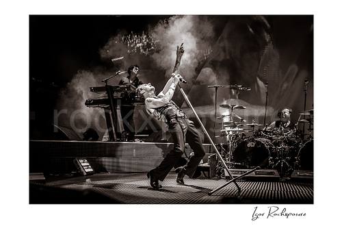 Horizontal B&W image of Depeche Mode members Peter Gordeno, Dave Gahan, and Christian Eigner performing on stage
