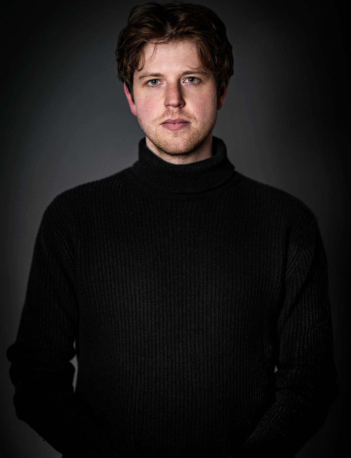 Portrait of a man in a black turtle neck top on a dark background.