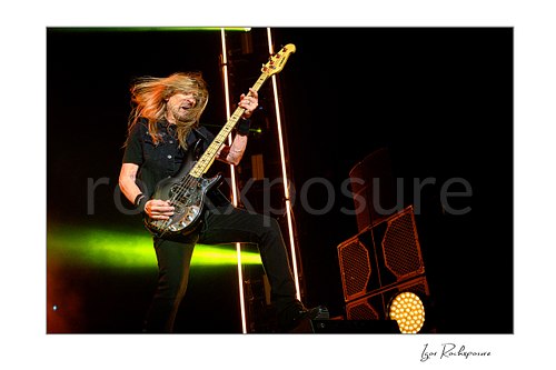 Horizontal color image of James LoMenzo of Megadeth playing bass on stage with flying hair and vivid concert lighting