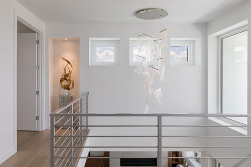 Architectural interior of a modern sculpture room in a Ponte Vedra beachfront home, featuring a dramatic contemporary glass chandelier, minimalist art displays, and high-end staging.