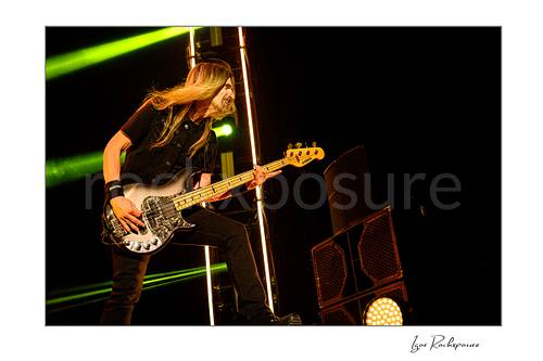 Horizontal color image of James LoMenzo of Megadeth playing bass on stage with long hair and green concert lights