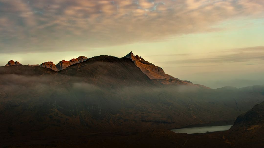 Mountain ridge at sunset on the Isle of Skye in Scotland with soft light and low cloud drifting through the valley.