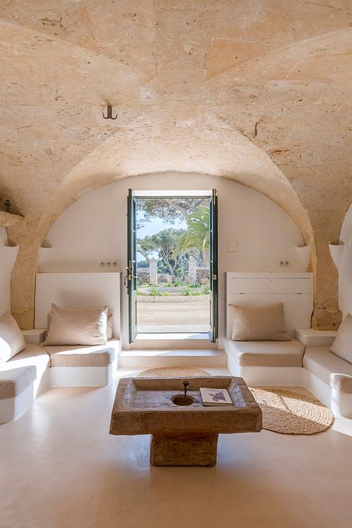 Salon voûté en pierre d’une finca d’agrotourisme à Santa Ponça, Minorque, avec banquettes et table centrale en pierre. Photographie par Nicolas Karadimos.