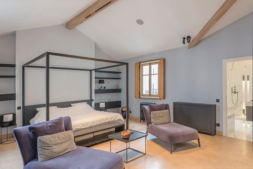 Chambre avec lit à baldaquin noir et poutres apparentes, offrant une vue sur la salle de bains en marbre, dans un appartement haussmannien sur les Champs-Élysées, Paris. Photographie d’architecture intérieure par Nicolas Karadimos.
