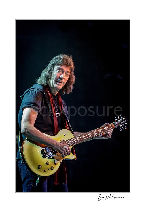 Vertical color image of Steve Hackett performing live with electric guitar in a close-up stage portrait