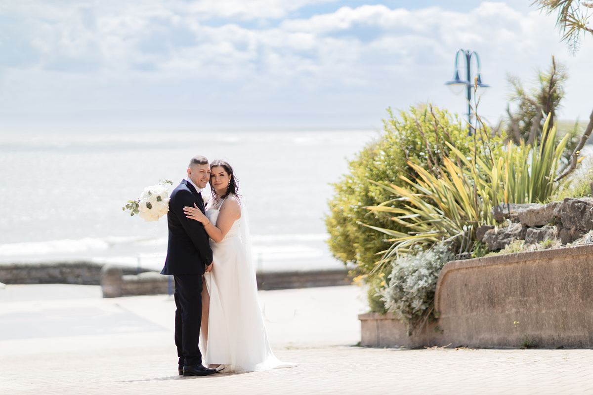 Bride and groom standing together with the sea in the background at Barry Island, South Wales
