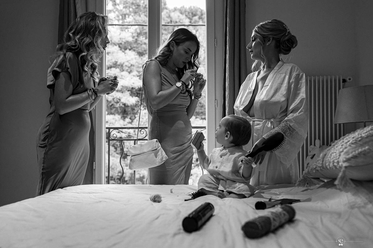 Sc&egrave;ne en noir et blanc d'une femme en robe verte aidant la mari&eacute;e &agrave; s'occuper de son enfant, avec des moments de complicit&eacute; et de soin maternel avant la c&eacute;r&eacute;monie &agrave; N&icirc;mes par S&eacute;bastien Clavel