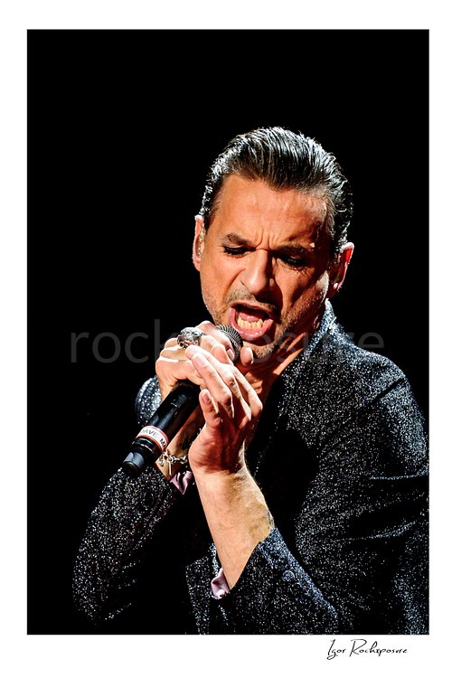 Vertical color image of Depeche Mode singer Dave Gahan singing into a microphone during a live performance
