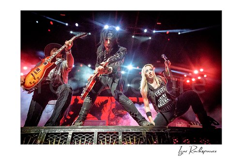 Horizontal color image of Ryan Roxie, Tommy Henriksen and Nita Strauss of the Alice Cooper Band performing live on stage with low-angle perspective, guitars, and bright red concert lighting