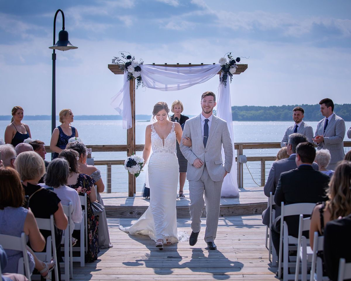 bride and groom walking down the aisle after the ceremony with the wedding arbor and rehoboth bay in the backgrond
