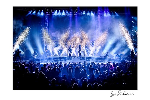 Horizontal color image of Trans Siberian Orchestra performing on stage with sparkling pyrotechnics, blue lighting, and a packed arena crowd