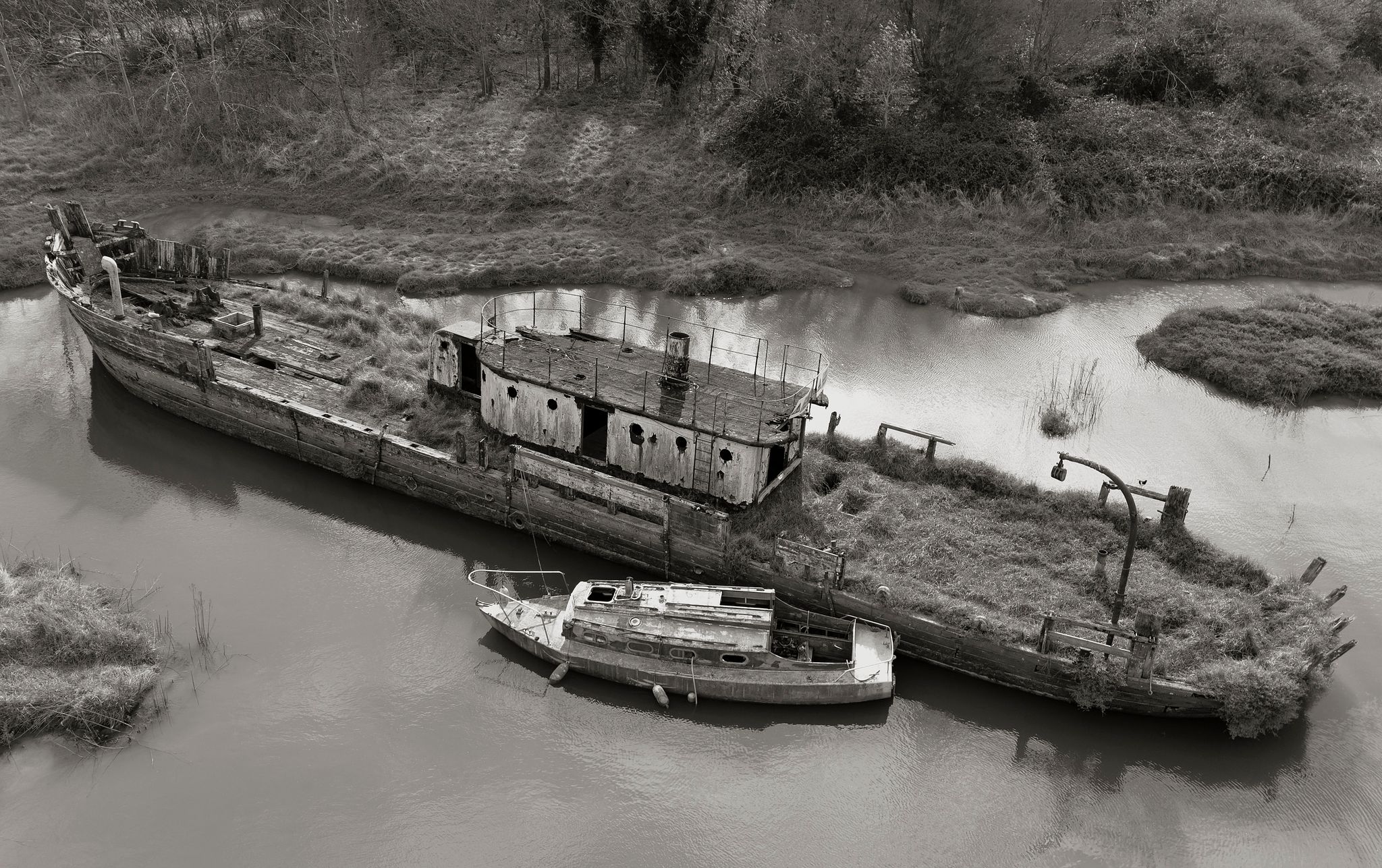 A timeless aerial view of endurance and the passage of time, where two weathered boats find solace in a quiet, winding Essex waterway﻿.
