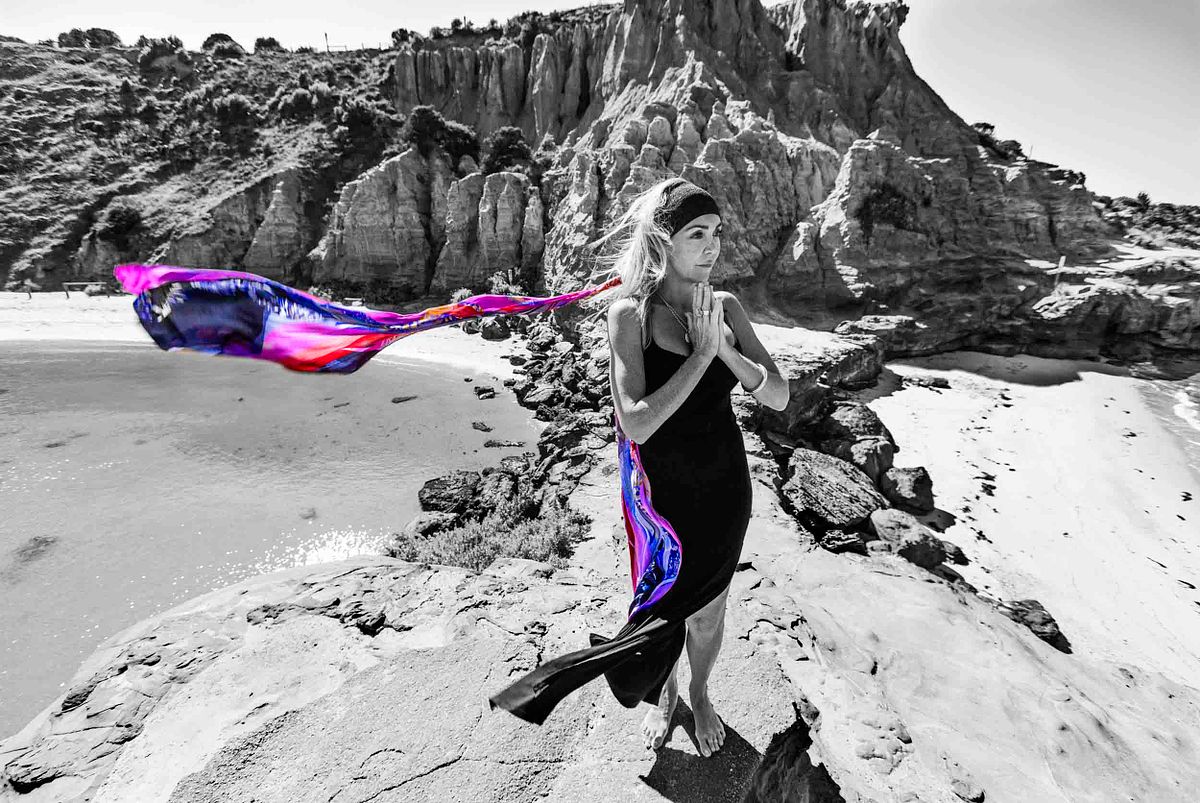 A black and white portrait of a woman standing on a cliff over looking the water, here scarfe is in colour.