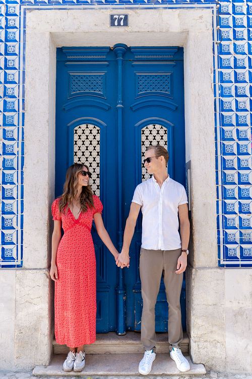Couple holding hands beside a blue tiled doorway in Lisbon