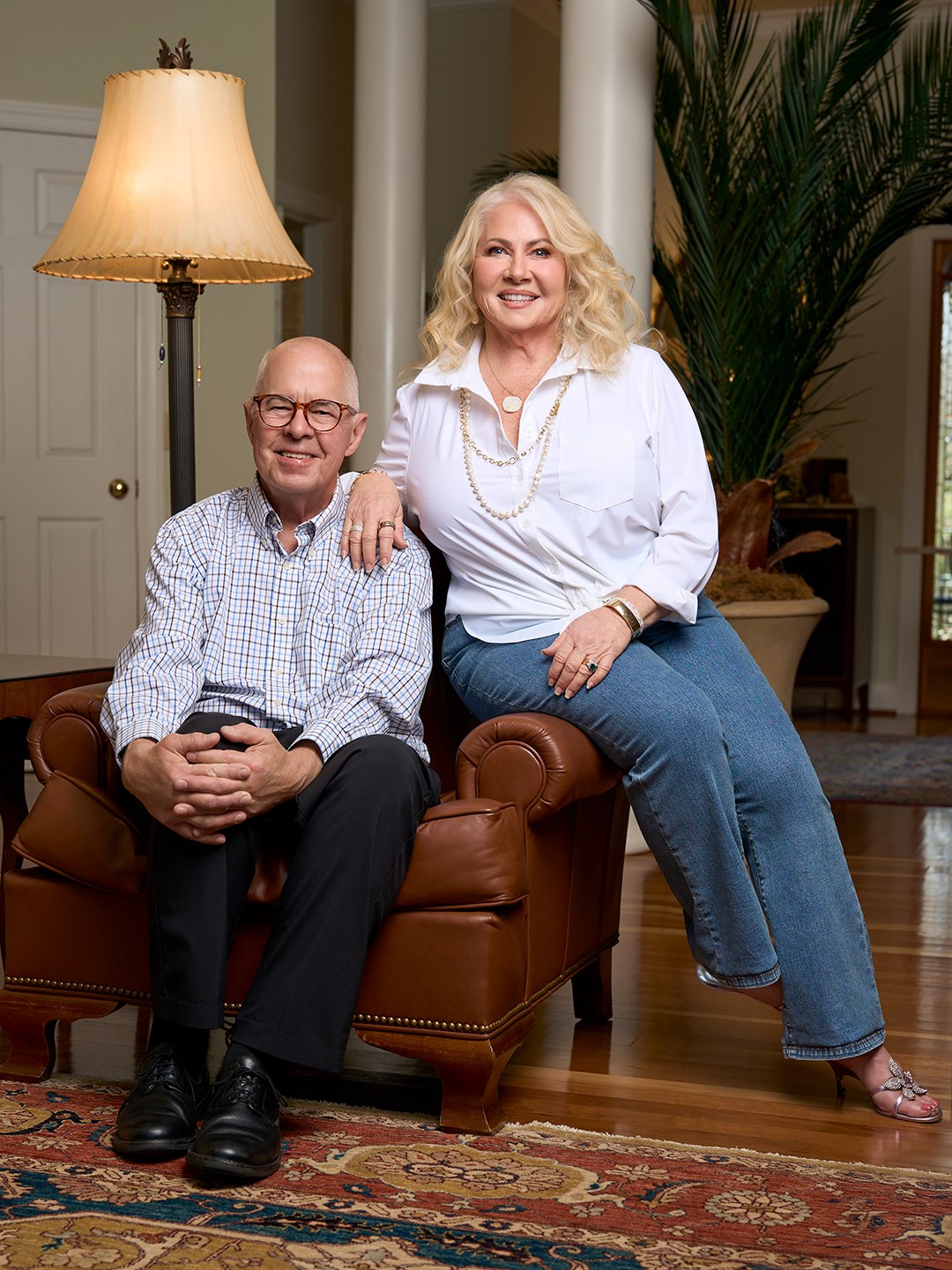 An older husband and wife pose for a relaxed but formal portrait inside their home.