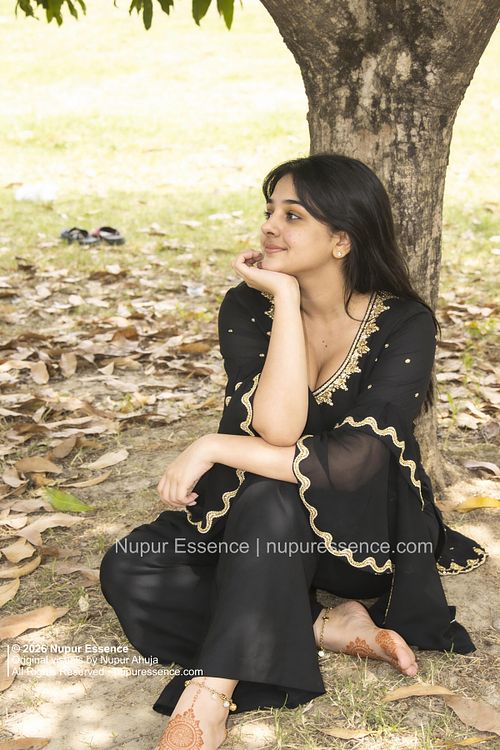 Nupur Ahuja for Nupur Essence sitting beneath a tree wearing a black ethnic outfit with gold accents