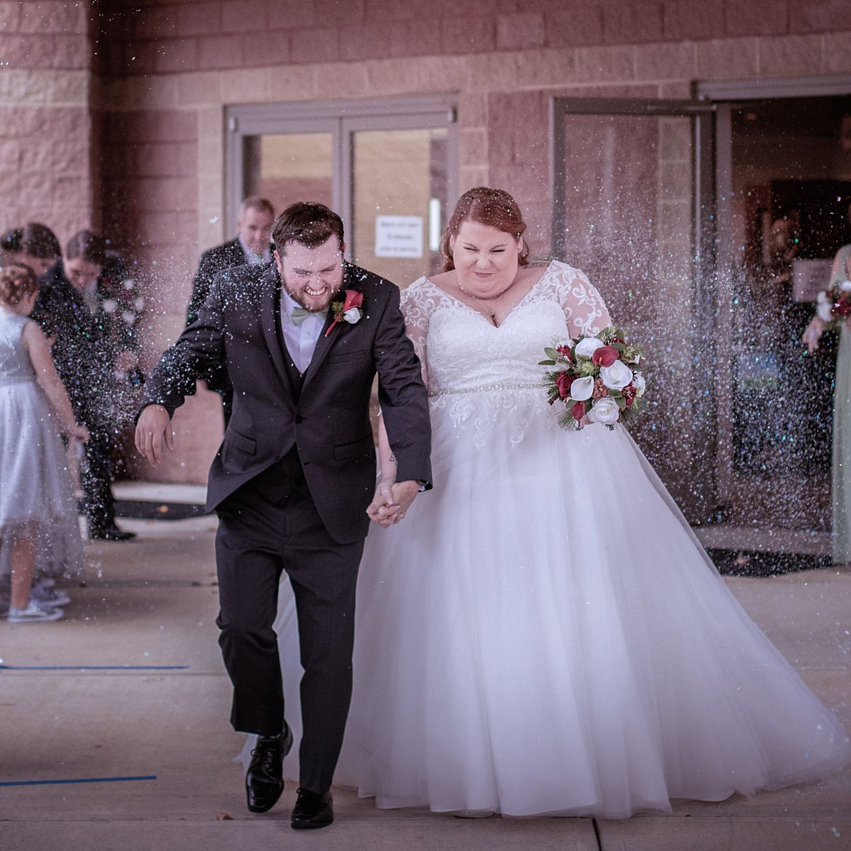 bride and groom leaving the church during a winter wedding in Salisbury, the guest are throwing rice at them and laughing