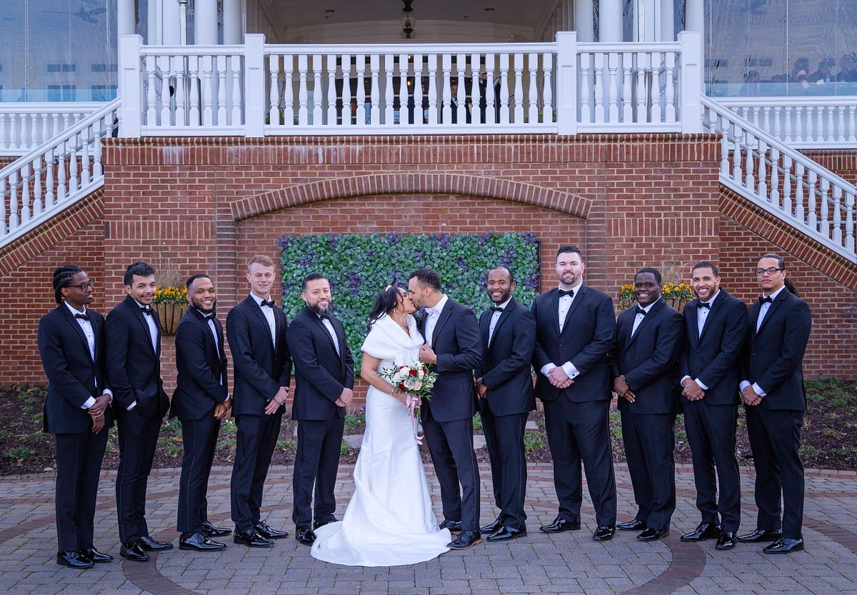 bride and groom kissing with groomsmen smiling