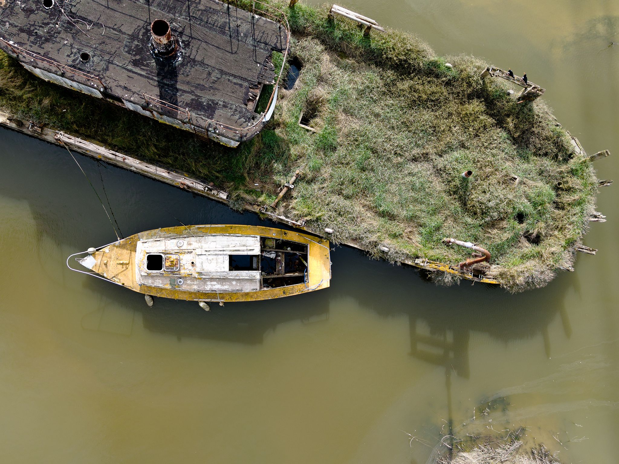Aerial photograph of two weathered boats moored in calm green coastal water