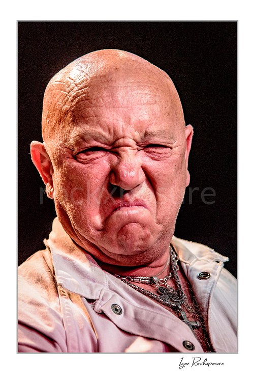 Vertical color image of Angry Anderson of Rose Tattoo in a tight onstage close-up with a fierce expression under warm concert light