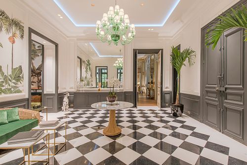 Salon d’un appartement haussmannien de 400 m² rue du Faubourg Saint-Honoré avec sol en damier noir et blanc, papier peint à motifs de palmiers et lustre vert. Photographie d’architecture intérieure par Nicolas Karadimos.