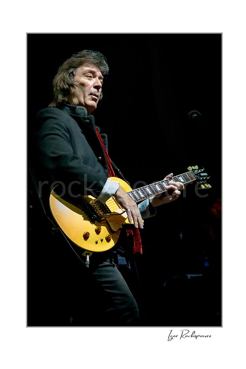 Vertical color image of Steve Hackett performing live with electric guitar in a close-up stage portrait