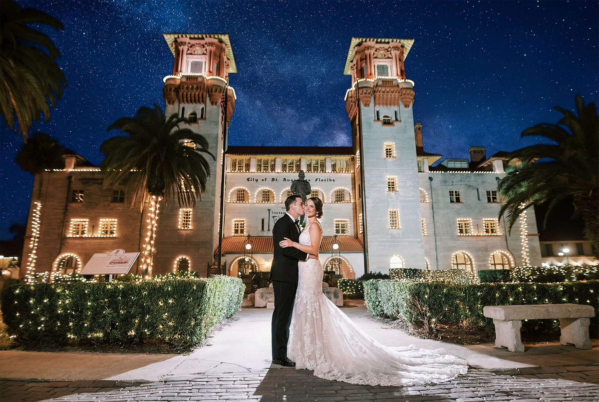 Bride and groom sharing a romantic kiss in front of the Lightner Museum at night, captured by Legacy of Love Photography in St. Augustine.