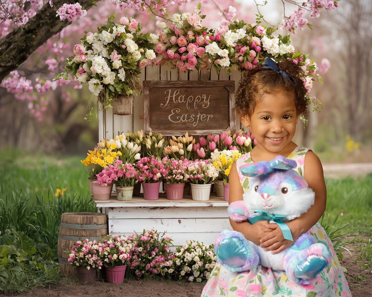 Young girl holding a plush Easter bunny in a spring flower garden during an Easter-themed children's portrait session.