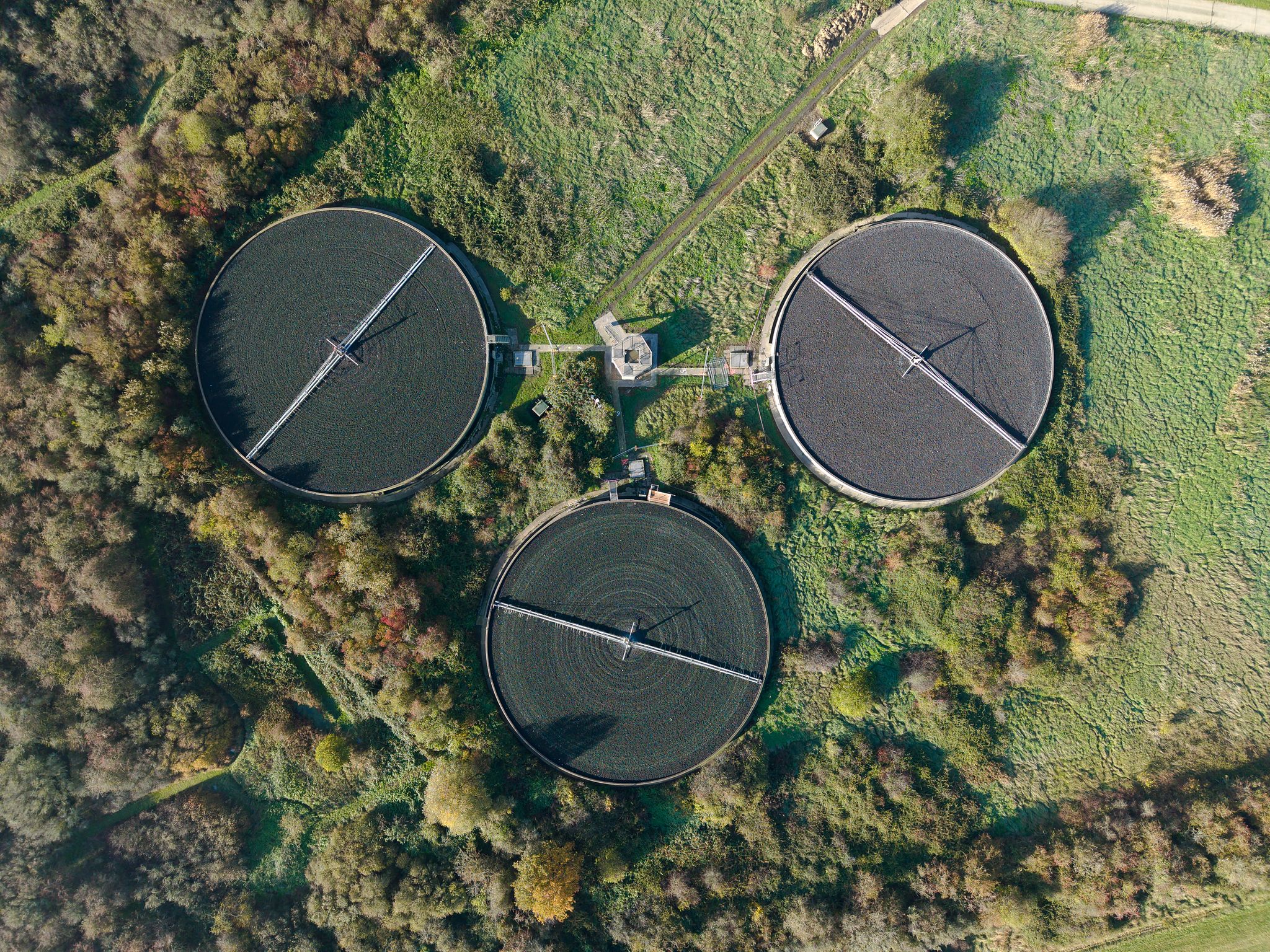 Aerial drone photograph of circular industrial settlement tanks surrounded by woodland and geometric landscape patterns