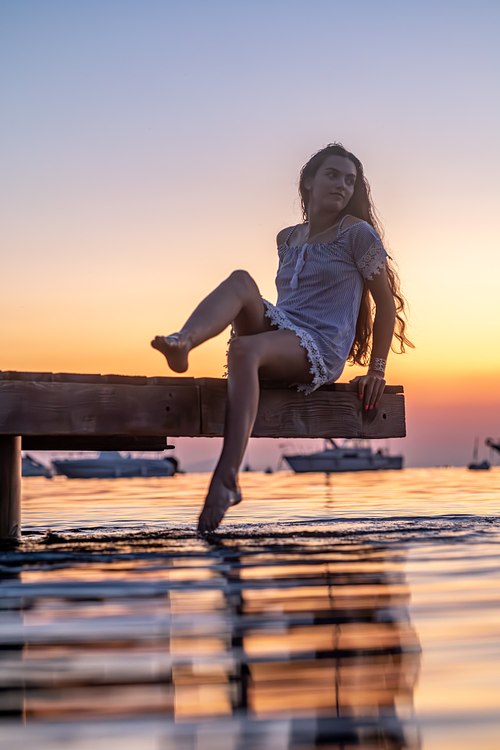 Femme assise sur un ponton avec les reflets du coucher de soleil dans la mer