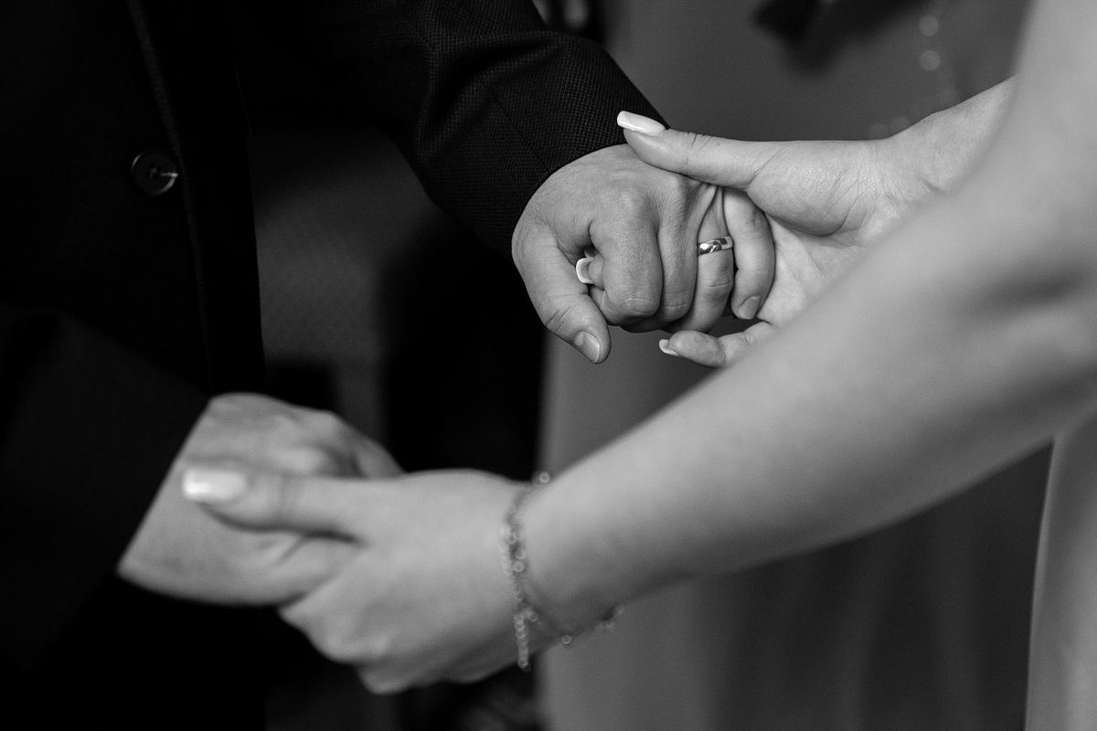 Black and white close-up of bride and groom holding hands with wedding rings visible
