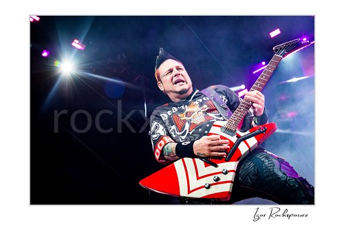 Horizontal color image of Zoltan Bathory of Five Finger Death Punch playing guitar under purple stage light and light concert haze