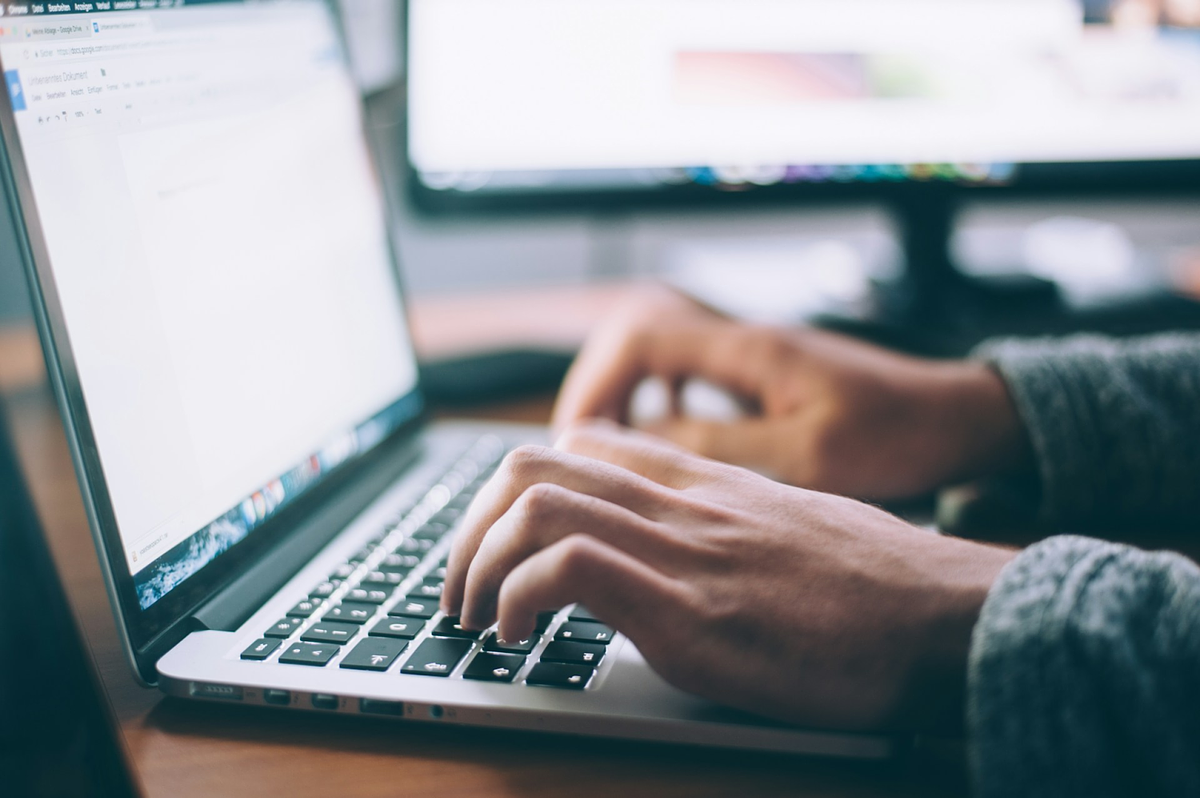 Persona escribiendo en un teclado portátil con un monitor de fondo
