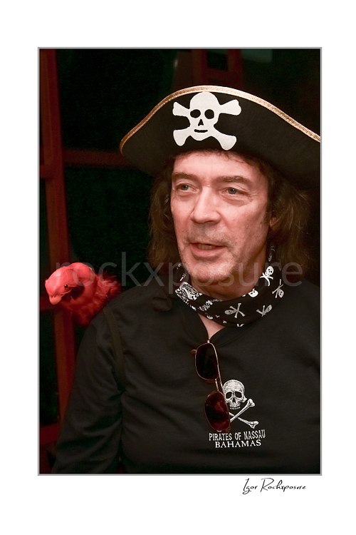 Vertical color image of Steve Hackett wearing a pirate hat with skull and crossbones and a red parrot on his shoulder