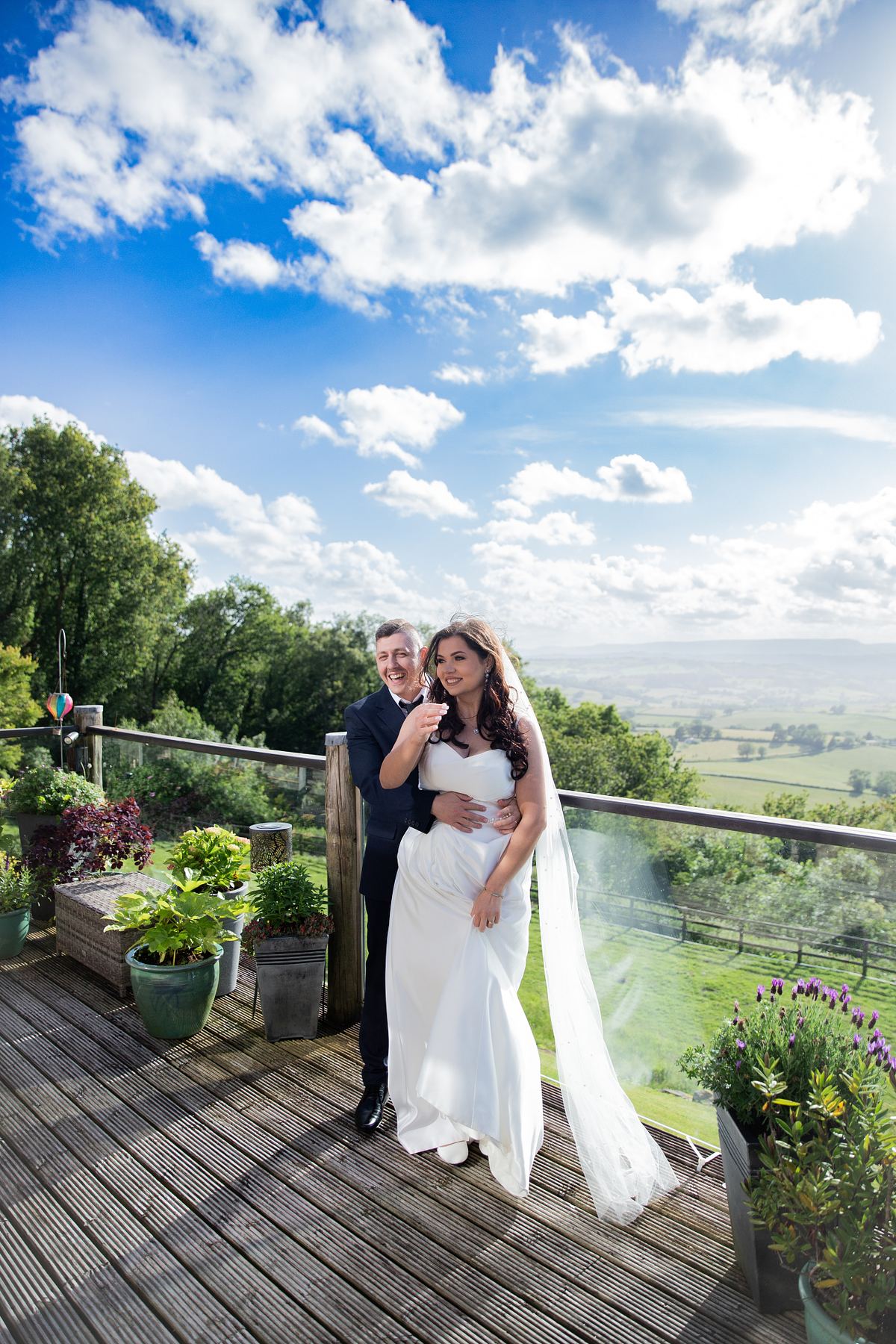 Bride and groom smiling together on a terrace with panoramic countryside views in South Wales