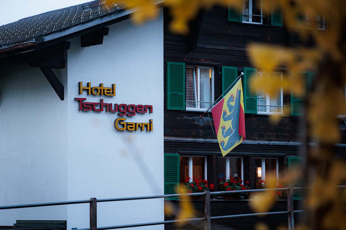 Fassade des Hotel Tschuggen Garni in Grindelwald mit dreidimensionaler Beschriftung, gr&uuml;nen Fensterl&auml;den, roten Geranien und der Berner Kantonsflagge