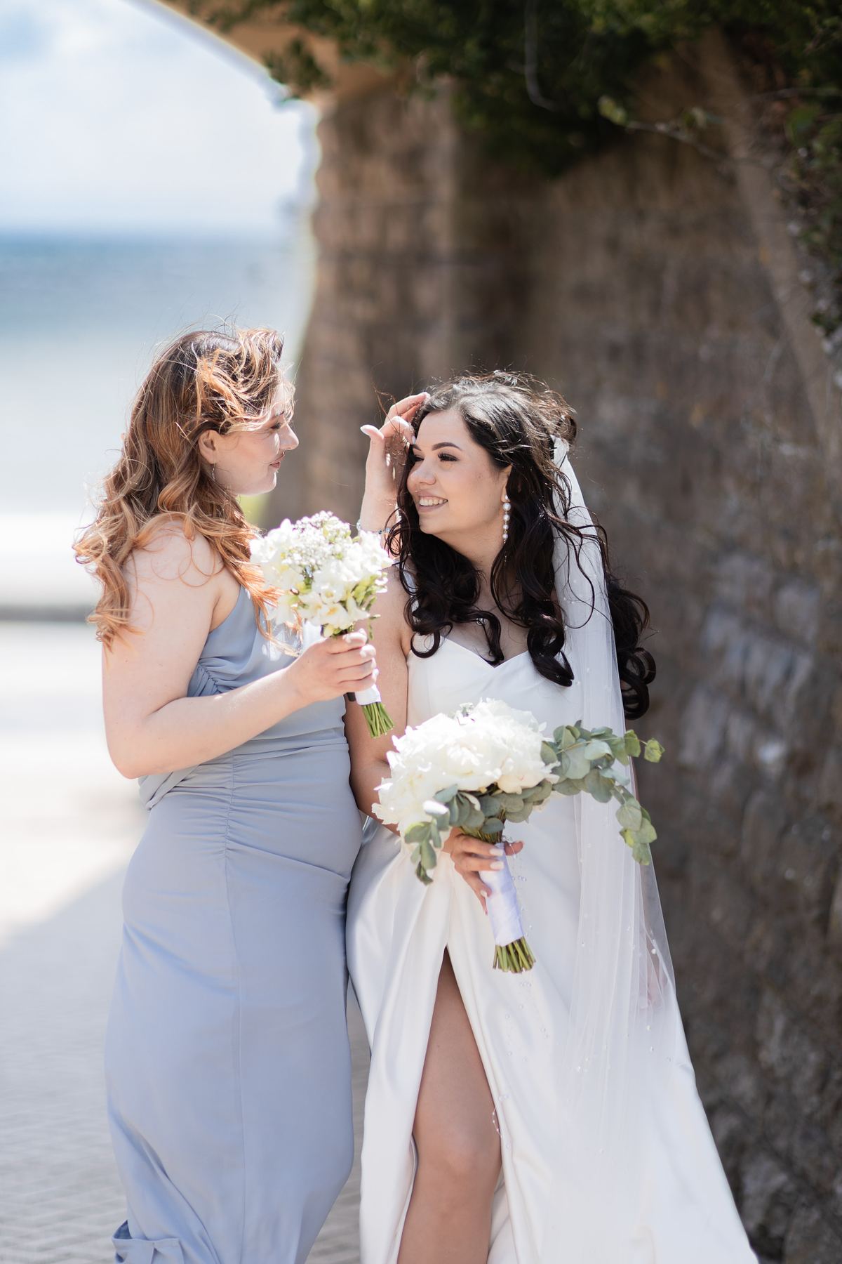 Bride smiling with bridesmaid beside the seafront at Barry Island, South Wales