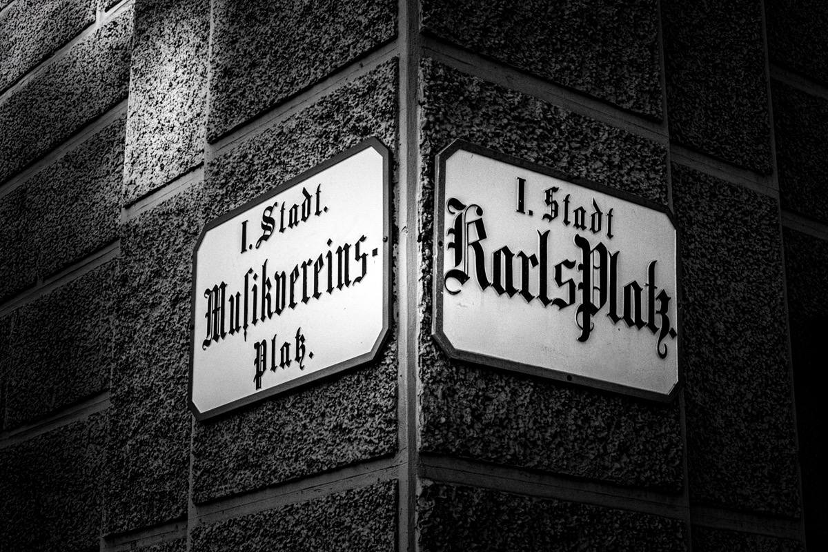Schwarz-Weiß-Fotografie von zwei Straßenschildern in Wien an einer Gebäudeecke