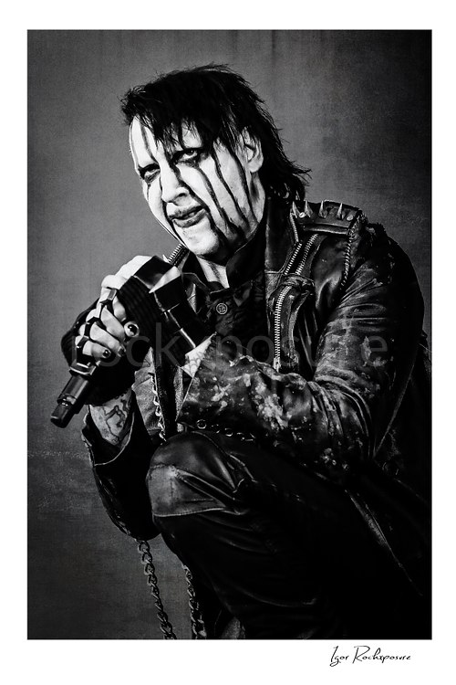 Vertical black and white image of Marilyn Manson holding a microphone in a tight theatrical portrait