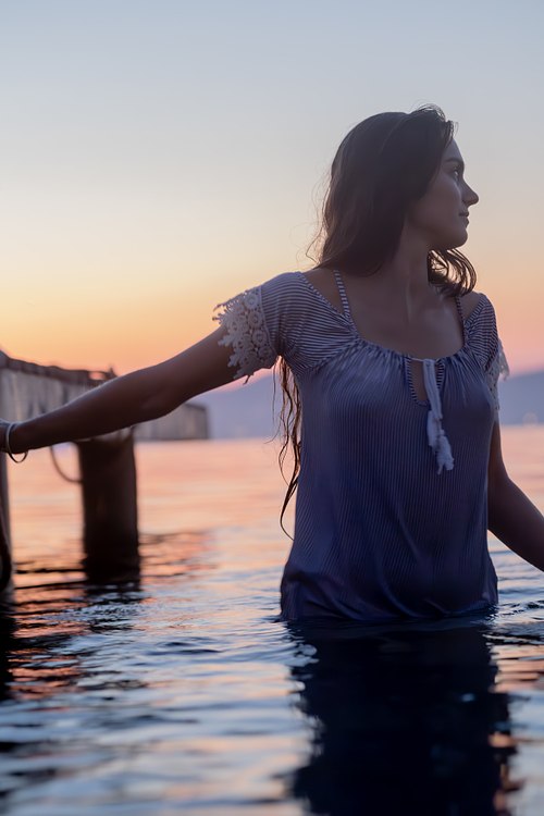 Femme debout dans la mer près d’un ponton avec le coucher de soleil en arrière-plan