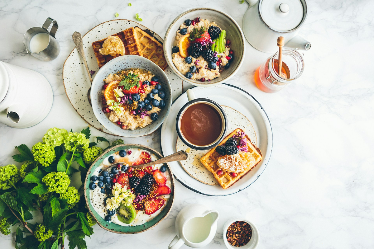 Un desayuno saludable que incluye gofres, tazones de fruta y té en una mesa de mármol blanco.