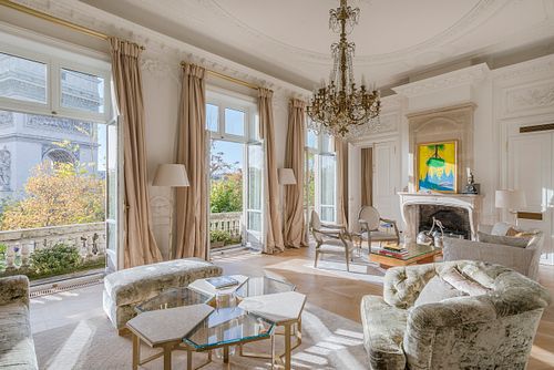 Salon haussmannien dans un immeuble de 1880 à la Place de l’Etoile, Paris, avec canapé gris, cheminée blanche et grande fenêtre. Photographie d’architecture intérieure par Nicolas Karadimos.